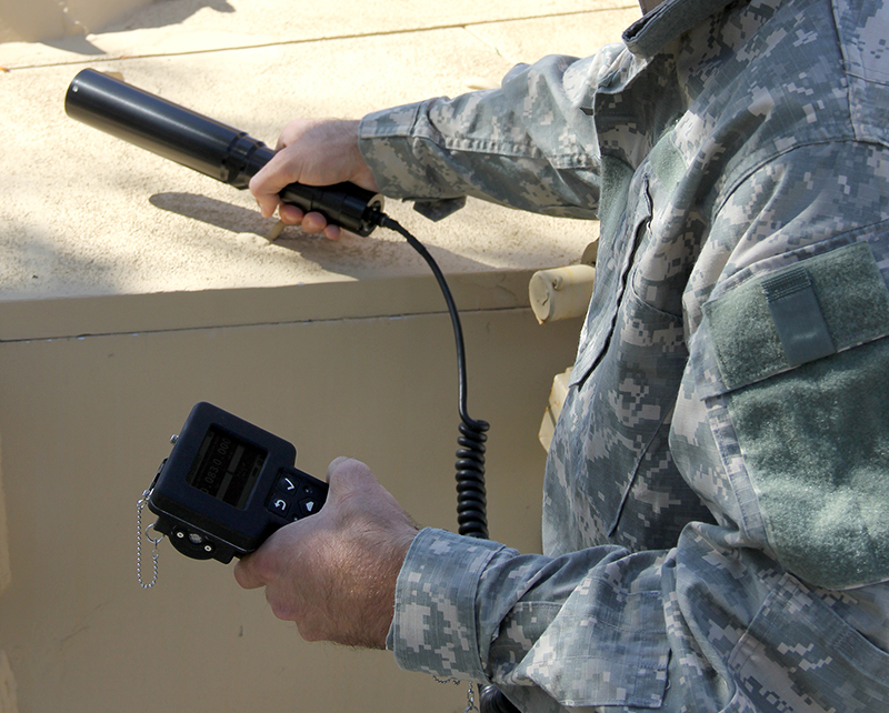Military person holding the RDS base unit and connected gamma probe to scan a surface